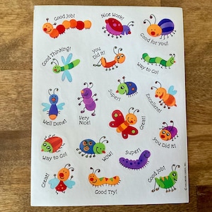 May include: Sheet of colorful stickers featuring cartoon insects with encouraging phrases like "Good Job!" and "Way to Go!" The stickers are in various colors and designs, perfect for rewarding achievements.