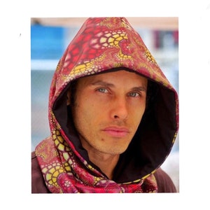 May include: A hooded scarf with a vibrant red, yellow, and black pattern. The hood and scarf are lined with a dark brown fabric. The design features an intricate, abstract print, creating a unique and eye-catching accessory.