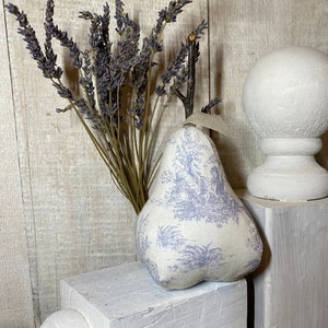 May include: A decorative pear-shaped fabric item with a blue toile pattern, next to a bundle of dried lavender and a white sphere on a pedestal. The pear has a beige stem and a fabric loop.