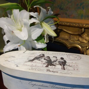 May include: An oval wooden box with a distressed white finish. The lid features a graphic of four birds on a musical staff with the text CARTE POSTALE and PARIS. The side displays the text Exposition Universelle PARIS 1889 GRAND PRIX.