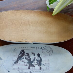 May include: An oval wooden box with a removable lid. The lid features a white distressed finish with a graphic print of four birds perched on musical notes, the text "CARTE POSTALE," and a circular "TOUR EIFFEL" postmark stamp.