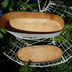 May include: An oval wooden box with a light-colored interior and a matching removable lid. The exterior is painted white with black text that reads "Grand Prix" and "Paris 1955" printed on the side of the container.