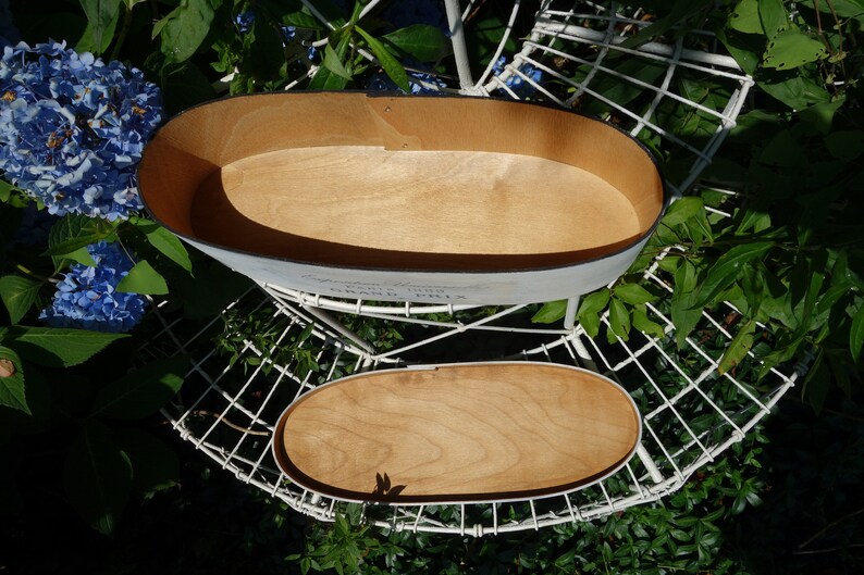 May include: An oval wooden box with a light-colored interior and a matching removable lid. The exterior is painted white with black text that reads "Grand Prix" and "Paris 1955" printed on the side of the container.