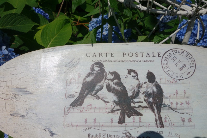 May include: An oval-shaped wooden plaque with a distressed white finish featuring a graphic of four birds perched on musical staff lines. The text reads CARTE POSTALE, Ce c&ocirc;t&eacute; est exclusivement r&eacute;serv&eacute; &agrave; l'adresse, and a circular stamp with 1909.