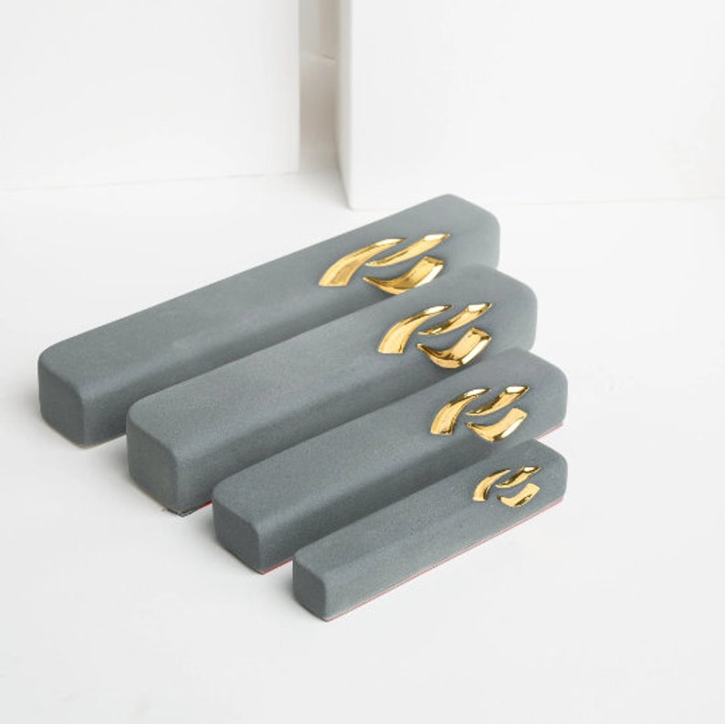 May include: Four gray rectangular decorative trays with gold accents. The trays are arranged in descending size order, with the largest tray at the top and the smallest tray at the bottom.