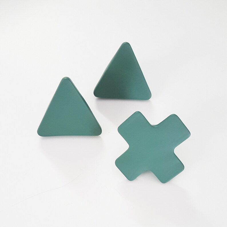 May include: Three wooden wall hooks in the shape of a triangle and a cross. The hooks are painted a muted teal green color.