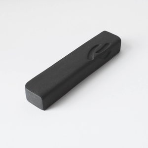 Puede incluir: Un palo de tinta rectangular negro con un diseño tallado en la parte superior.