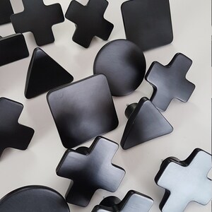 May include: A set of 15 black geometric wall hooks in various shapes, including circles, squares, triangles, and crosses. The hooks are made of wood and have a matte finish.