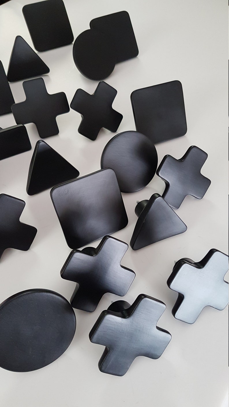 May include: A set of 15 black geometric wall hooks in various shapes, including circles, squares, triangles, and crosses. The hooks are made of wood and have a matte finish.