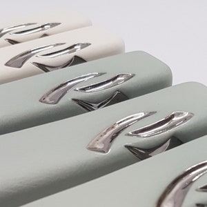 May include: Close-up of four rectangular ceramic drawer pulls with a silver metallic finish. The pulls have a curved design with a raised, stylized letter 'R' on each.
