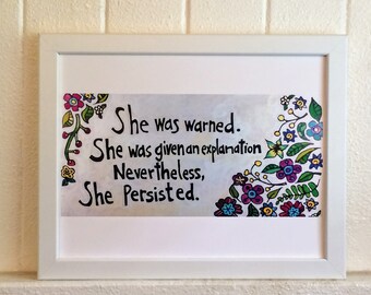 Puede incluir: Una impresión enmarcada en blanco con un borde floral colorido. La impresión presenta el texto "She was warned. She was given an explanation. Nevertheless, She Persisted."