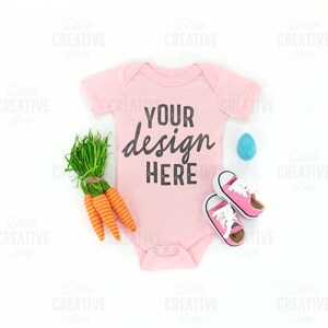 May include: Pink baby onesie with the text "YOUR design HERE" on a white background with carrots, a blue egg, and pink shoes.