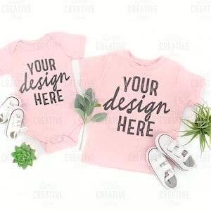 May include: Two pink baby t-shirts with the text "Your design here" on a white background with white trainers and green plants.