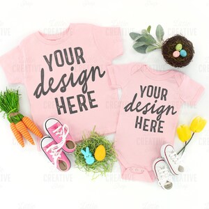 May include: Two pink t-shirts with the text "Your design here" on them. The shirts are laid out on a white background with other Easter-themed decorations, including a nest with eggs, carrots, and flowers.
