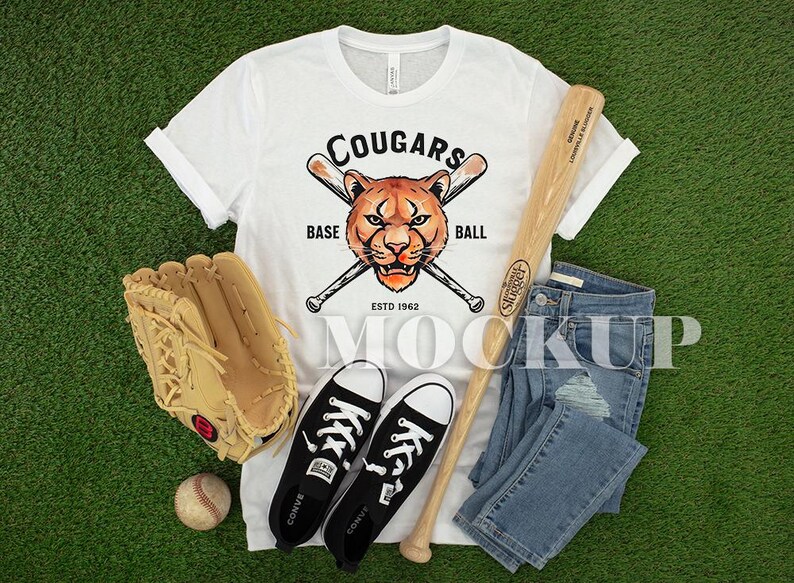 May include: White t-shirt with a cougar head and baseball bats graphic, baseball bat, baseball glove, baseball, black Converse trainers, and blue jeans on a green surface. The shirt says "Cougars Base Ball Estd 1962".