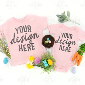 May include: Two pink shirts with the text "YOUR design HERE" on them. The shirts are surrounded by Easter decorations, including a nest with eggs, carrots, and flowers.