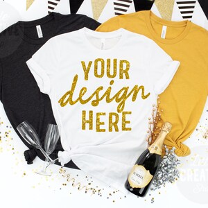 May include: Three t-shirts in black, white, and mustard yellow with the text "YOUR design HERE" in gold glitter on the white shirt. The shirts are arranged on a white surface with gold and silver confetti, a bottle of champagne, and two champagne flutes.