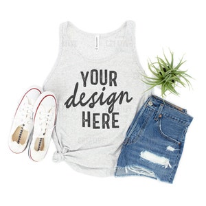 May include: A gray tank top with the text 'YOUR design HERE' on it. The tank top is laying on a white surface with a pair of white sneakers, a pair of blue denim shorts, and a green plant.
