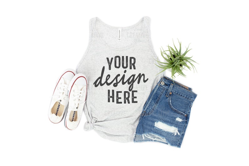May include: A gray tank top with the text 'YOUR design HERE' on it. The tank top is laying on a white surface with a pair of white sneakers, a pair of blue denim shorts, and a green plant.