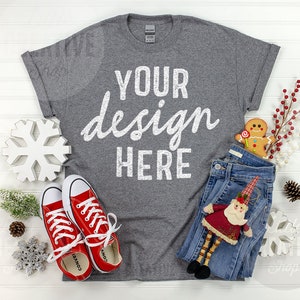 May include: A gray t-shirt with the text "YOUR design HERE" in white. The shirt is laid flat on a white wood background with red sneakers, blue jeans, a gingerbread man, and a small Santa figurine.
