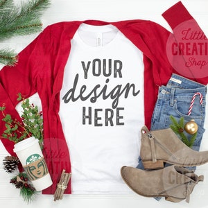 May include: White long-sleeve t-shirt with the text "YOUR design HERE" in black. The t-shirt is styled with a red cardigan, blue jeans, brown ankle boots, and holiday decor.