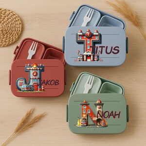 Könnte beinhalten: Vier farbenfrohe Lunchboxen mit Deckeln, jeweils mit einem einzigartigen Design. Die Boxen sind in Rot-, Blau- und Grüntönen gehalten und haben weiße Gabeln. Jede Box hat einen Namen und eine Feuerwehrgrafik.
