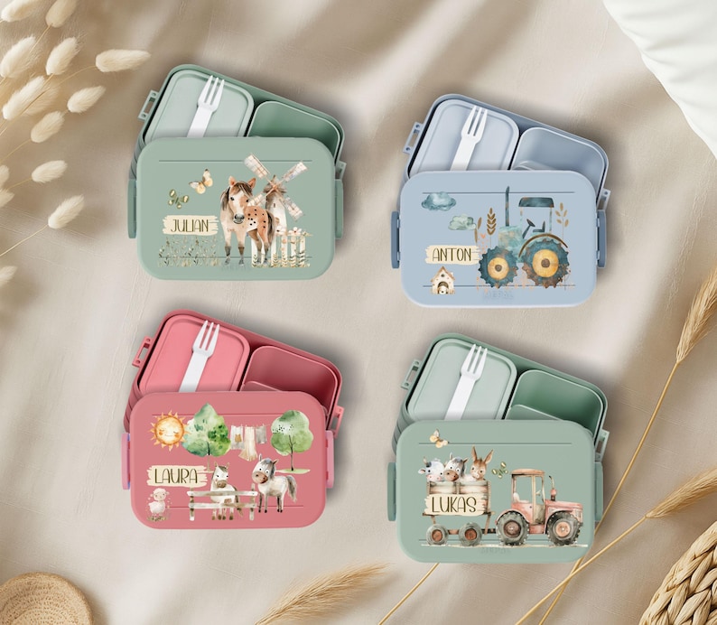 May include: Four colorful lunchboxes with different animal and farm themes. Each lunchbox has a name on it: Julian, Anton, Laura, and Lukas. The lunchboxes are made of durable plastic and have a built-in fork.