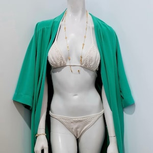 May include: A white swimsuit with a green robe. The swimsuit has a lace design and the robe has a long sleeve.