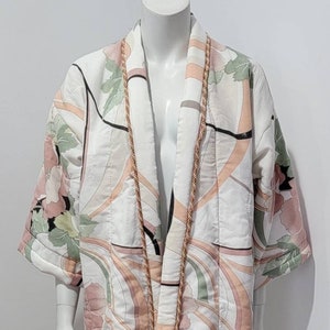 May include: A white quilted robe with a floral pattern and a gold trim. The robe has a long, flowing silhouette and is perfect for lounging around the house.