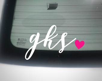 May include: White vinyl decal with the letters "gks" in a cursive font, accompanied by a small, bright pink heart. The decal is designed to be applied to a car window.