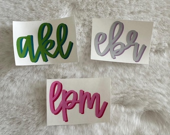 Op de afbeelding: Drie rechthoekige stickers met aangepaste letters in een cursief handschrift. Eén sticker toont de letters akl in het groen, één toont ebr in lichtpaars en één bevat lpm in felroze. Elke letter is voorzien van een donkerder schaduweffect.