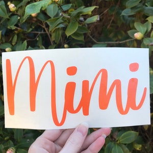 May include: Orange vinyl decal with the word "Mimi" written in a cursive font.