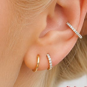 May include: A set of three earrings worn on an ear: one plain gold-toned hoop, one small pavé hoop with clear stones, and one larger pavé hoop cuff. The text reads: Sterling silver pave hoops. For plain hoops find link below.