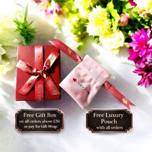 a red gift box with a red ribbon, placed on a table with a bouquet of flowers in the background. There are two signs in the image, one indicating a free gift box and the other offering a free luxury pouch with all orders above £50 or paying for a gift wrap.