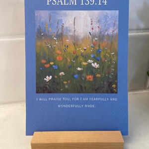 Könnte beinhalten: Blaue Karte mit dem Text "PSALM 139:14" und einem farbenfrohen Blumenbild. Der Text "I WILL PRAISE YOU, FOR I AM FEARFULLY AND WONDERFULLY MADE" ist ebenfalls enthalten. Die Karte steht auf einem Holzständer.