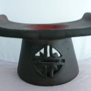 May include: A black ceramic pedestal with a red interior and a carved design on the base. The pedestal is shaped like a crescent moon and is used for displaying objects.