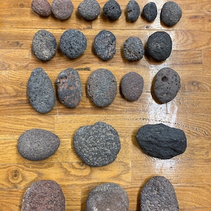 May include: An assortment of various-sized, porous lava rocks in shades of gray, brown, and black. The rocks are arranged on a wooden surface, showcasing their unique textures and shapes. Ideal for decorative purposes or landscaping.