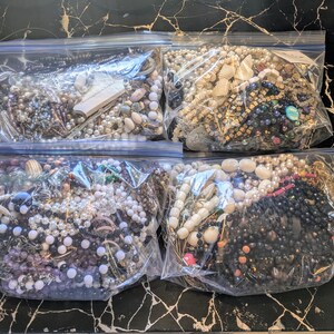 May include: Four clear plastic bags filled with various necklaces, bracelets, and beads. The jewelry includes pearls, beads, and other decorative elements in a variety of colors. Some bags have tags.