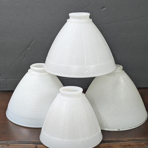 May include: Four white glass lampshades with different textured patterns. The lampshades are cone-shaped and have a white frosted finish.