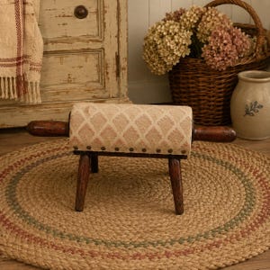 May include: A small bench featuring a seat made from a repurposed wooden rolling pin with a beige and white diamond pattern fabric cushion. The bench has four dark brown wooden legs and is secured with a row of metal upholstery tacks.