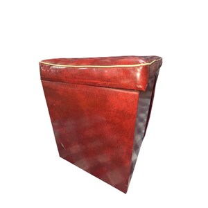 Puede incluir: Un otom&aacute;n rectangular rojo con una parte superior acolchada y un ribete dorado. Los lados son de color rojo liso y el interior es visible. El otom&aacute;n es de estilo vintage.