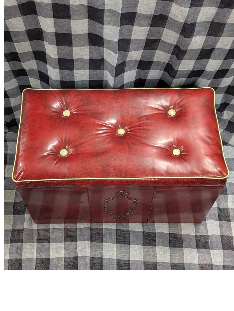 Puede incluir: Un otom&aacute;n rectangular rojo con una parte superior acolchada y botones dorados. Los bordes est&aacute;n adornados con un borde dorado. La parte delantera del otom&aacute;n presenta un dise&ntilde;o decorativo de peque&ntilde;os tachuelas redondas.