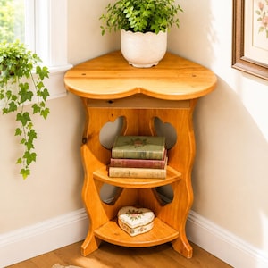 May include: A wooden corner shelf with three tiers, holding books and a heart-shaped trinket box. A potted plant sits on top. The shelf is made of light-colored wood and has decorative heart-shaped cutouts.