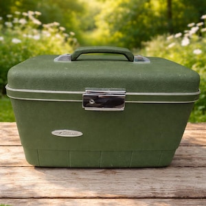 May include: A vintage olive green travel case with a silver clasp and handle. The case has a textured surface and a white trim. The case is sitting on a wooden surface.