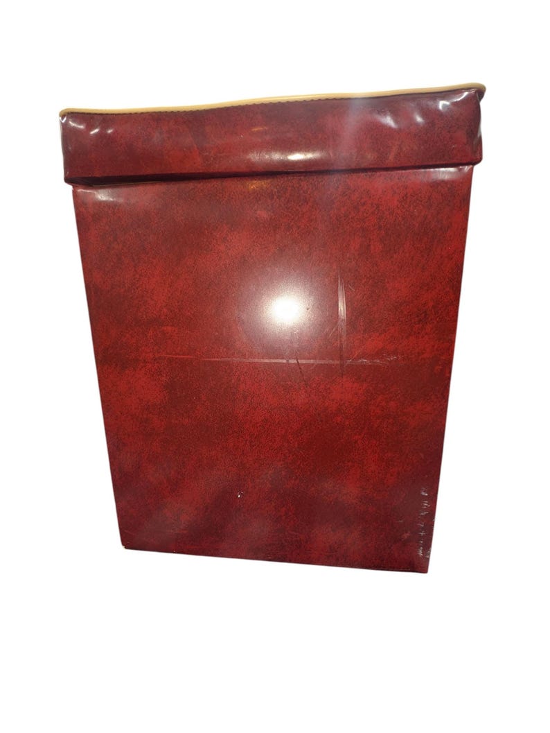 Puede incluir: Una caja rectangular roja con una superficie texturizada. El borde superior est&aacute; doblado y tiene un ribete dorado. La caja est&aacute; hecha de un material que parece ser cuero o similar al cuero.