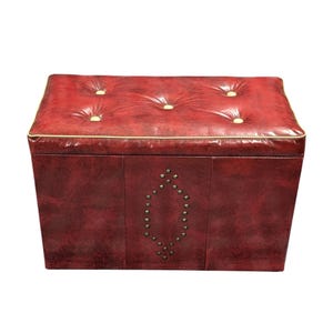 Puede incluir: Un otom&aacute;n rectangular de cuero rojo con una parte superior acolchada y botones dorados. Los bordes est&aacute;n ribeteados con un borde dorado. La parte delantera presenta un dise&ntilde;o en forma de diamante con peque&ntilde;os tachuelas plateadas.