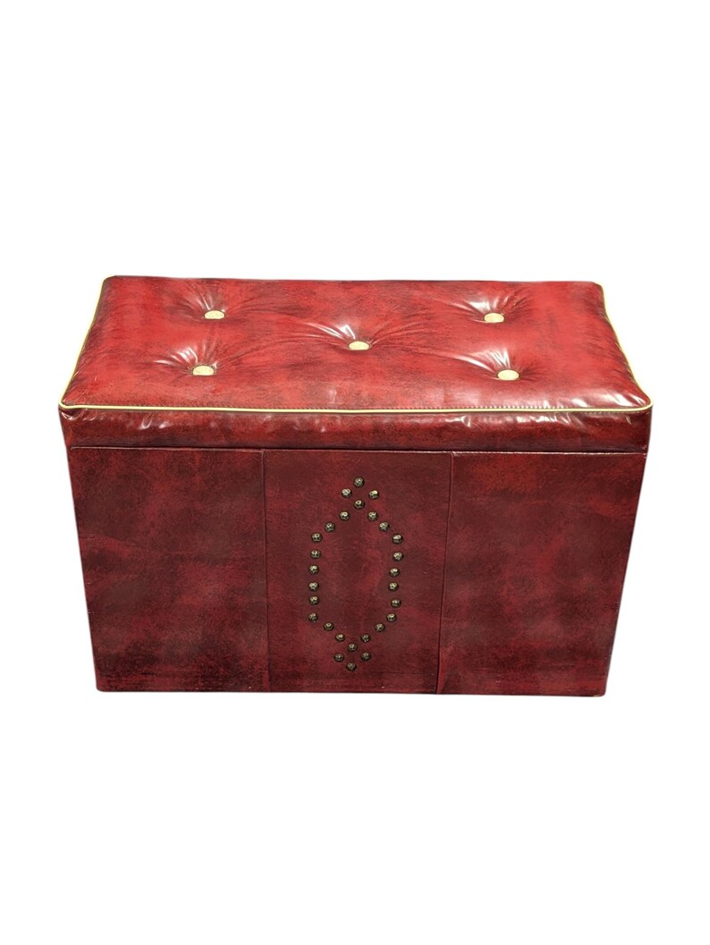 Puede incluir: Un otom&aacute;n rectangular de cuero rojo con una parte superior acolchada y botones dorados. Los bordes est&aacute;n ribeteados con un borde dorado. La parte delantera presenta un dise&ntilde;o en forma de diamante con peque&ntilde;os tachuelas plateadas.