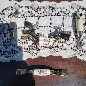 May include: Five decorative cabinet knobs with floral designs. The knobs are made of white porcelain with gold accents and feature a variety of floral patterns in shades of pink, blue, and green.