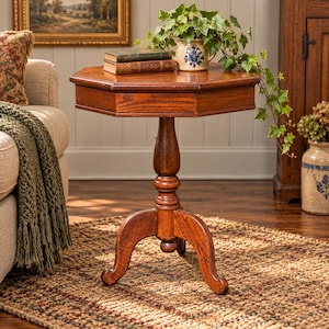 May include: An octagonal wooden side table with a pedestal base and three curved legs. The table features a rich brown wood grain finish and a smooth top surface. The central column is turned with decorative detailing, providing a stable foundation.