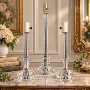 May include: Three clear glass lamp bases with faceted crystal-like circular bases and vertical ribbed stems. The central lamp base is taller than the two flanking it, and each features a metallic socket at the top for light bulb installation.